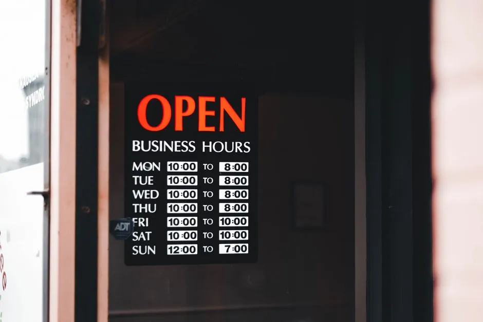 Store hours signage posted in a shop window, illustrative stock photo